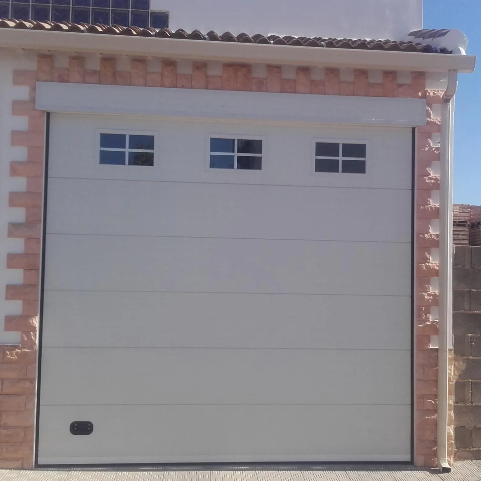 Puerta seccional automática en panel sándwich blanco con ventanas superiores, fabricada por Carpintería Metálica Toni en San Pedro, Albacete