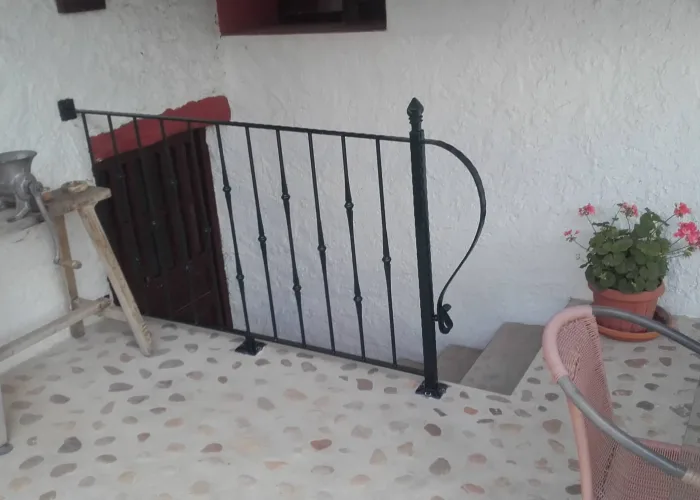 Barandilla de hierro con detalle curvo en extremo, instalada por Carpintería Metálica Toni en San Pedro, Albacete, para cierre de escalera interior en vivienda rústica.