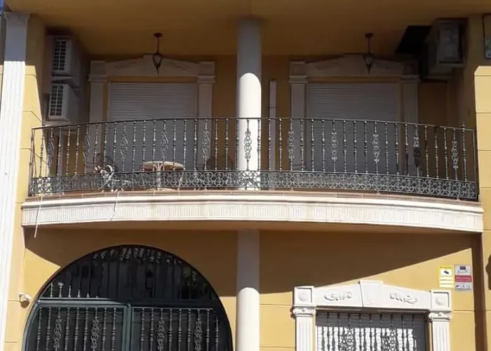 Fachada de vivienda con barandilla, reja y portón de hierro forjado fabricados por Carpintería Metálica Toni en San Pedro, Albacete. Diseño ornamental con acabados clásicos para balcones, ventanas y entrada de cochera.