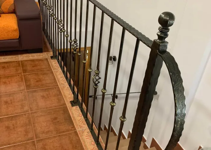 Barandilla interior de hierro forjado instalada en vivienda, fabricada por Carpintería Metálica Toni en San Pedro, Albacete. Diseño artesanal con pasamanos texturizado y detalles decorativos en latón.