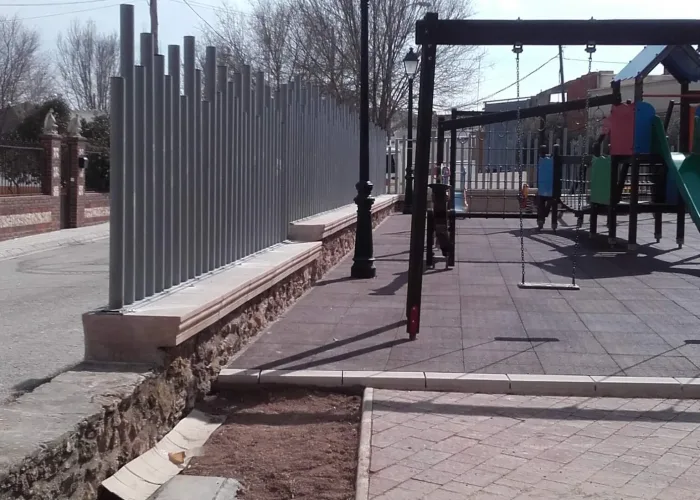 Cerramiento metálico para parque infantil fabricado por Carpintería Metálica Toni en San Pedro, Albacete, con diseño moderno en varilla redonda de diferentes alturas sobre muro de piedra.