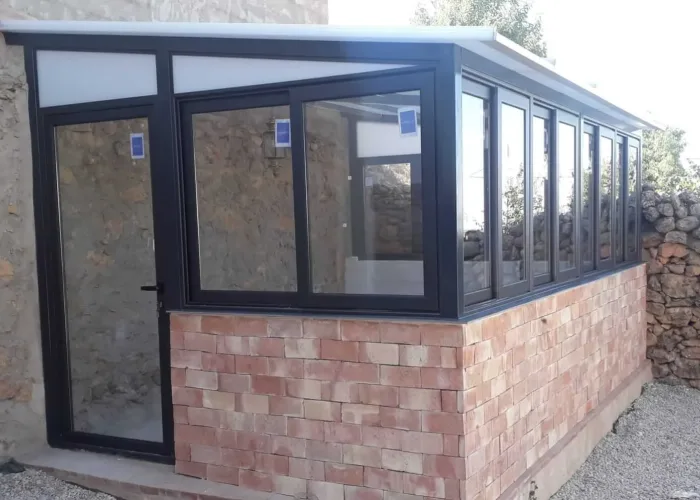 Cerramiento de terraza con perfilería de aluminio en color negro, acristalamiento completo y zócalo de ladrillo visto, fabricado por Carpintería Metálica Toni en San Pedro, Albacete