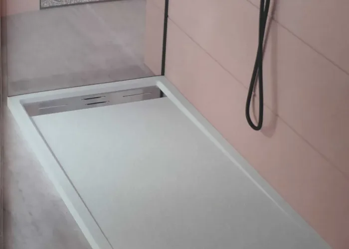 Plato de ducha rectangular en color blanco con textura antideslizante y rejilla metálica lateral, instalado con grifería negra mate en un baño de pared rosa. Trabajo realizado por Carpintería Metálica Toni en San Pedro, Albacete.