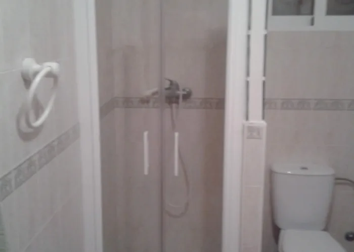 Mampara de ducha abatible en cristal templado transparente con tiradores blancos, instalada en baño pequeño con azulejo beige y separación de pavés, fabricada por Carpintería Metálica Toni en San Pedro, Albacete.