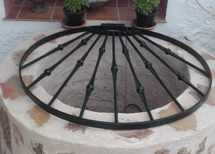 Rejilla de forja circular para pozo, elaborada por Carpintería Metálica Toni en San Pedro (Albacete). Diseñada para ofrecer seguridad sin renunciar a la estética tradicional, con barrotes torneados y estructura resistente, perfecta para viviendas rurales o patios con encanto rústico.