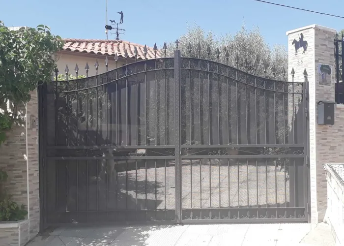 Puerta de forja clásica con acabado en negro y remates ornamentales, fabricada por Carpintería Metálica Toni en San Pedro (Albacete). Un diseño robusto y elegante que aporta seguridad y distinción a la entrada de la vivienda. Ideal para entornos residenciales con estética tradicional o rústica.