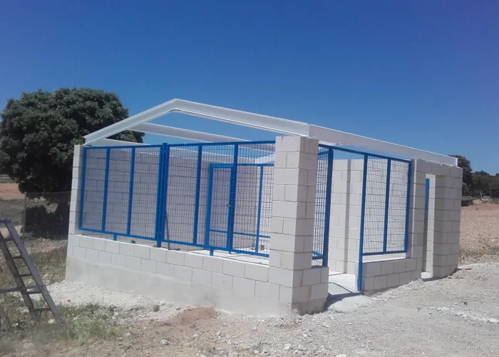 Estructura metálica con cerramiento perimetral en malla electrosoldada azul, realizada por Carpintería Metálica Toni en San Pedro, Albacete, sobre base de bloque de hormigón. Ideal para uso ganadero o almacén rural.