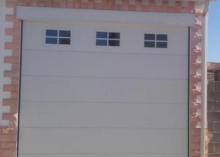 Puerta seccional automática en panel sándwich blanco con ventanas superiores, fabricada por Carpintería Metálica Toni en San Pedro, Albacete