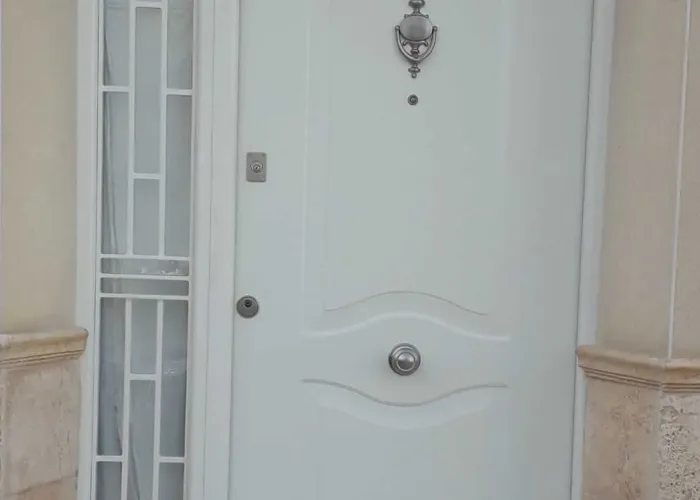 Puerta de entrada en aluminio blanco con diseño clásico, tirador redondo y panel lateral con reja decorativa, fabricada por Carpintería Metálica Toni en San Pedro, Albacete