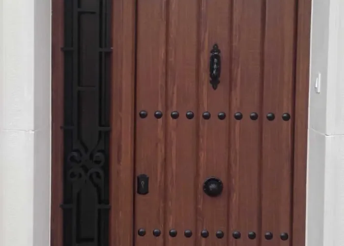Puerta de entrada en aluminio imitación madera con clavos decorativos y reja ornamental lateral y superior, fabricada por Carpintería Metálica Toni en San Pedro, Albacete