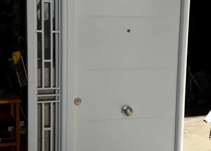 Puerta de entrada en aluminio blanco con diseño clásico, tirador redondo y panel lateral con reja decorativa, fabricada por Carpintería Metálica Toni en San Pedro, Albacete