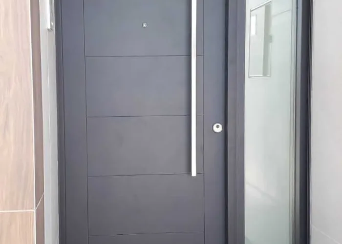 Puerta de entrada en aluminio gris oscuro con diseño moderno, tirador vertical de acero y panel lateral acristalado, fabricada por Carpintería Metálica Toni en Albacete