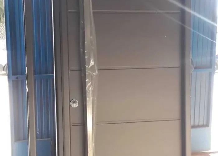Puerta de entrada en aluminio gris oscuro con diseño moderno, tirador vertical de acero y panel lateral acristalado, fabricada por Carpintería Metálica Toni en Albacete