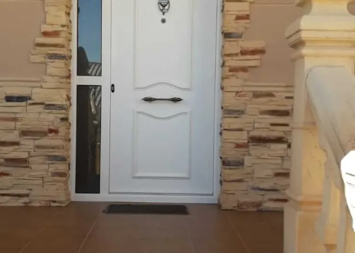 Puerta de entrada blanca de aluminio con panel lateral acristalado y decoraciones clásicas, instalada por Carpintería Metálica Toni en vivienda unifamiliar de Albacete