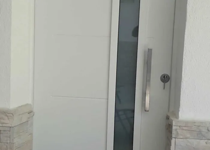 Puerta de entrada moderna en aluminio blanco con cristal vertical decorativo, fabricada por Carpintería Metálica Toni en Albacete