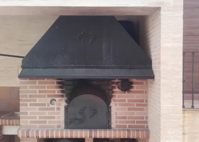 Horno de leña de obra con campana metálica decorativa y puerta de hierro, fabricado por Carpintería Metálica Toni en San Pedro, Albacete