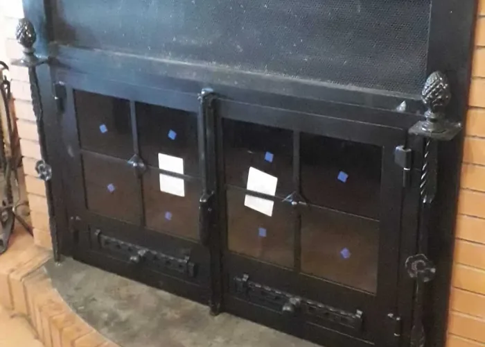 Puerta metálica de chimenea con doble hoja de vidrio y detalles de forja, fabricada por Carpintería Metálica Toni en San Pedro, Albacete