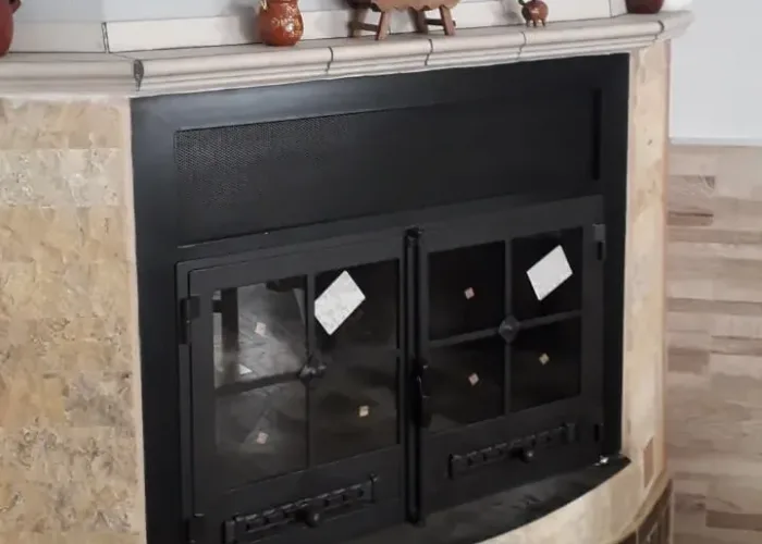 Puerta metálica de chimenea curva con doble hoja de cristal y rejilla superior, fabricada por Carpintería Metálica Toni en San Pedro, Albacete