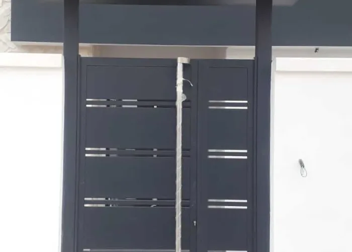 Puerta exterior metálica de diseño moderno con lamas horizontales y acabado en negro mate, fabricada por Carpintería Metálica Toni en San Pedro, Albacete. Instalación con marquesina superior y estructura robusta.