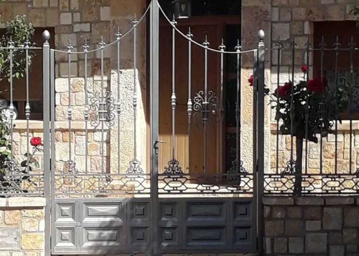 Puerta de acceso peatonal en forja artística con remates curvos y detalles ornamentales, elaborada por Carpintería Metálica Toni en San Pedro (Albacete). Un diseño elegante que aporta carácter y distinción a viviendas con fachada de piedra. Seguridad con un toque clásico y decorativo.