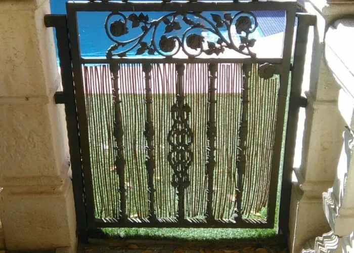 Puerta pequeña de forja artística para acceso a jardín o piscina, con detalles florales y acabados decorativos. Fabricada por Carpintería Metálica Toni en San Pedro (Albacete), ideal para delimitar espacios exteriores con un toque clásico y elegante.