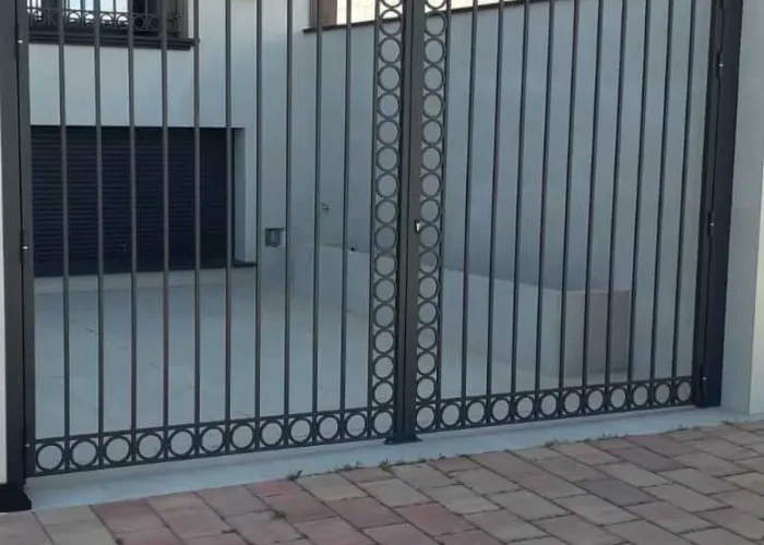Puerta metálica de entrada a vivienda con diseño de barrotes verticales y detalles de círculos decorativos, fabricada por Carpintería Metálica Toni en San Pedro, Albacete. Acabado elegante y funcional, ideal para accesos a patios y garajes.