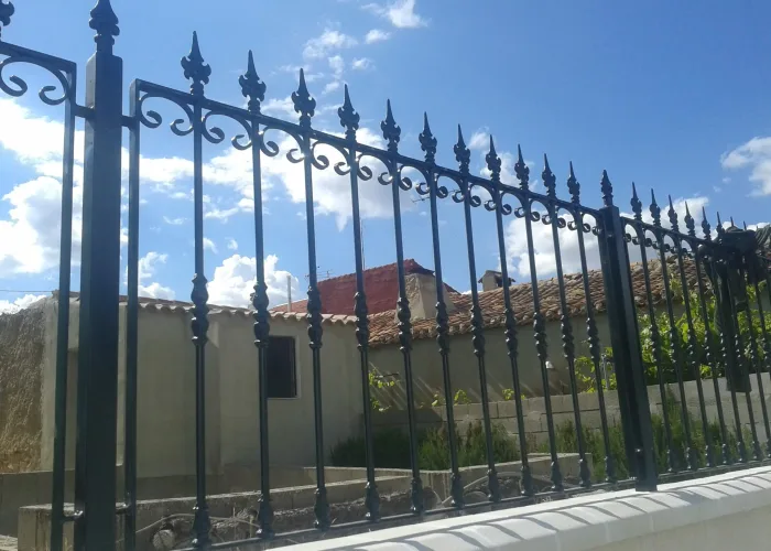 Valla metálica de forja tradicional con remates en punta de lanza y elementos decorativos curvos. Fabricación robusta realizada por Carpintería Metálica Toni en San Pedro (Albacete), ideal para delimitar parcelas con un toque clásico y elegante sin renunciar a la seguridad.